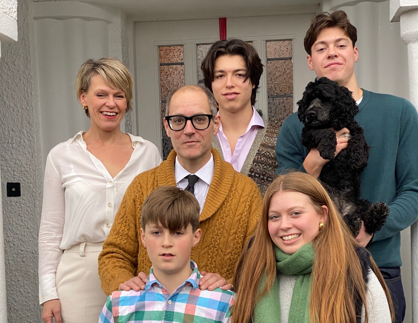 Family portrait of six people and a dog posing in a doorway.