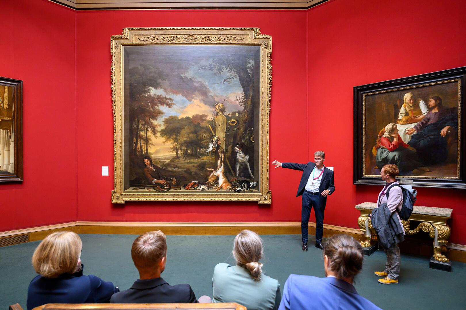 A tour guide lecturing a group of people in front of a large painting at the National Portrait Gallery Edinburgh.