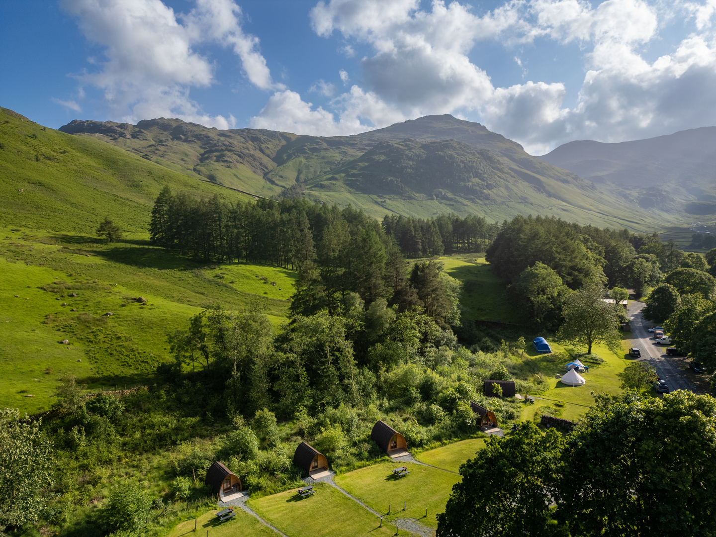 Aerial view of cabins and campsites nestled in a green valley surrounded by mountains.