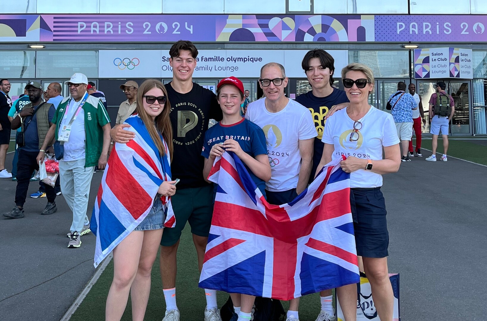 Family posing with a Union Jack flag in front of the Paris 2024 Olympic Games signage.