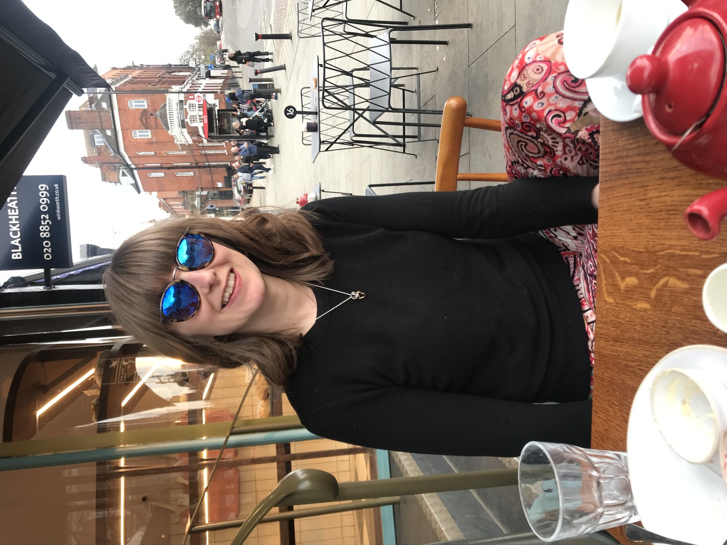 Woman wearing sunglasses sitting at an outdoor cafe table.