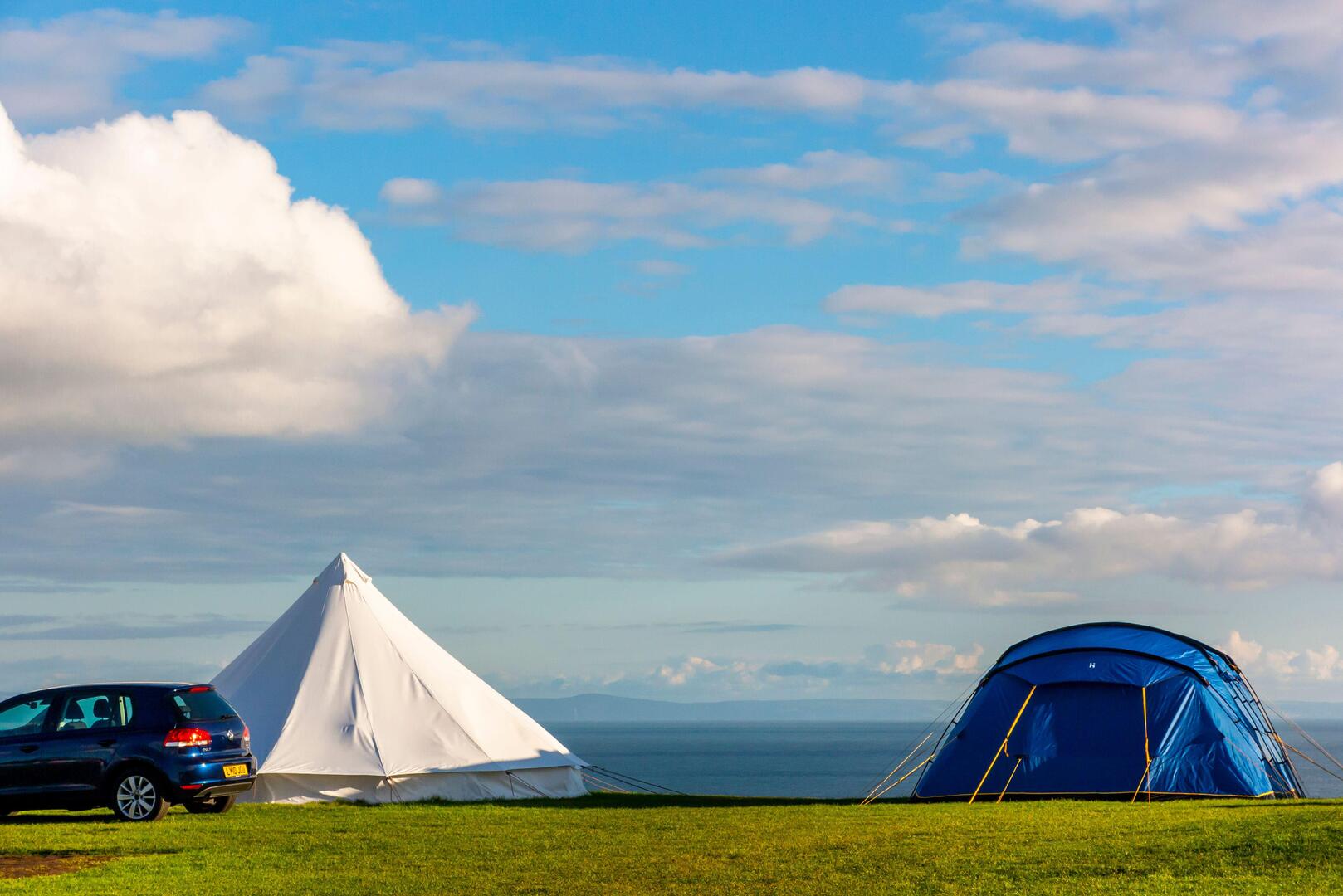 Clifftop campsite with tents and car overlooking the sea.