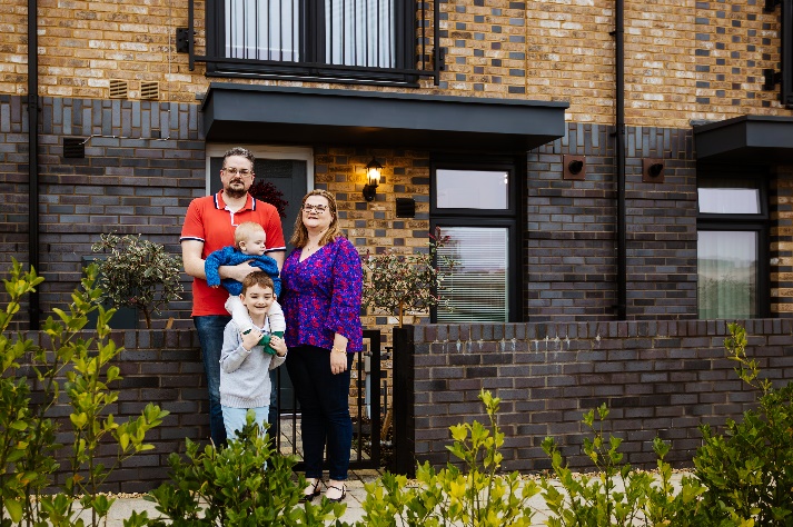 Family of four standing in front of their new home.