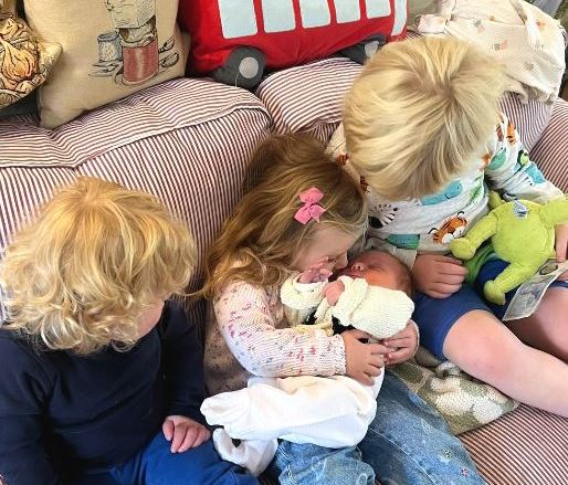 Three children cuddling a newborn baby.